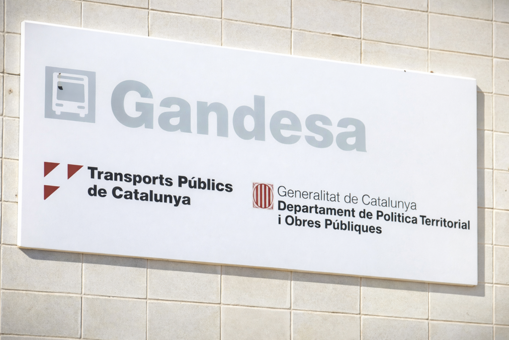 Placa de l'estació de bus de Gandesa amb els logotips de Transports Públics de Catalunya i la Generalitat de Catalunya.