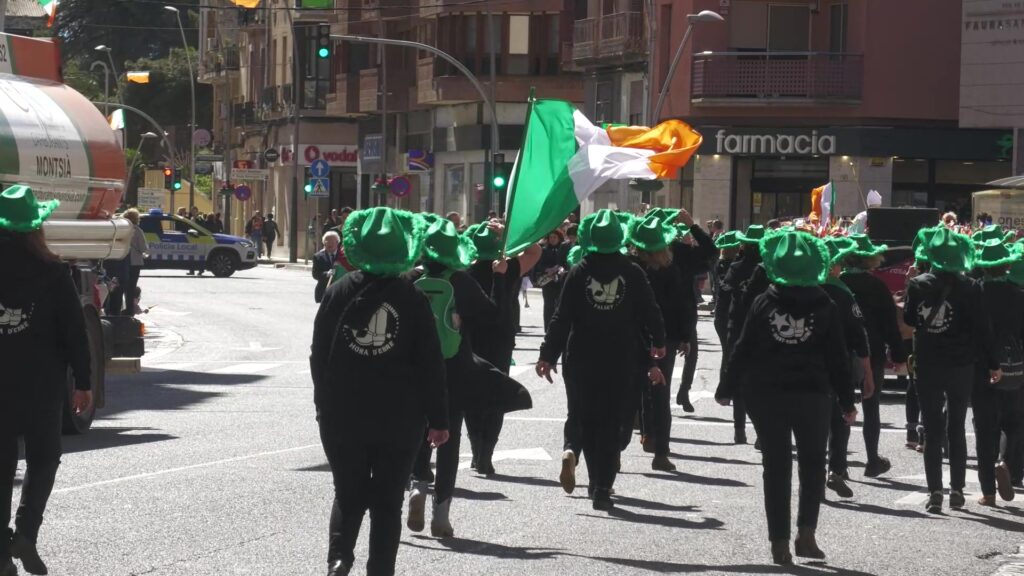 Participants vestits de negre i amb barrets verds desfilant amb una bandera d'Irlanda pel centre de Tortosa, al Baix Ebre.