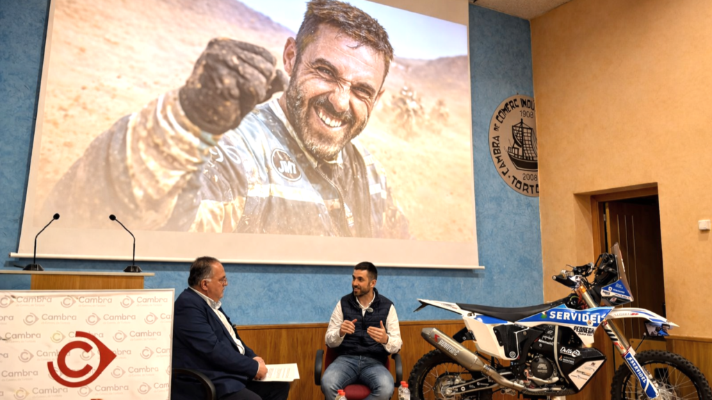 Joan Guillén en una conferència a la Cambra de Comerç de Tortosa amb la seua moto del Dakar.