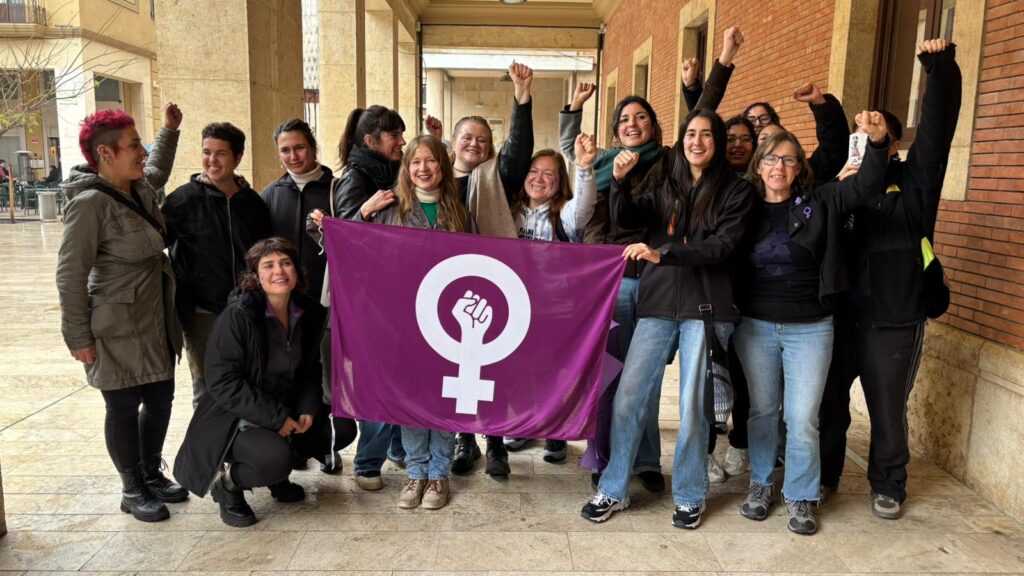 Grup de dones del col·lectiu Males Herbes amb una bandera feminista lila