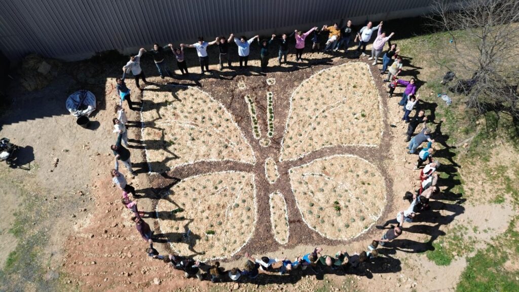 Voluntaris agafats de les mans rodejant una escultura en forma de papallona feta amb plantes a Amposta, Montsià.