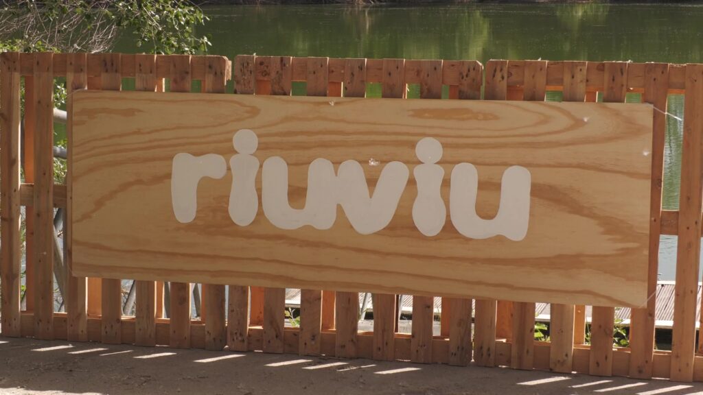 Cartell de fusta amb el logotip del festival Riuviu a la vora de l'Ebre a Aldover.
