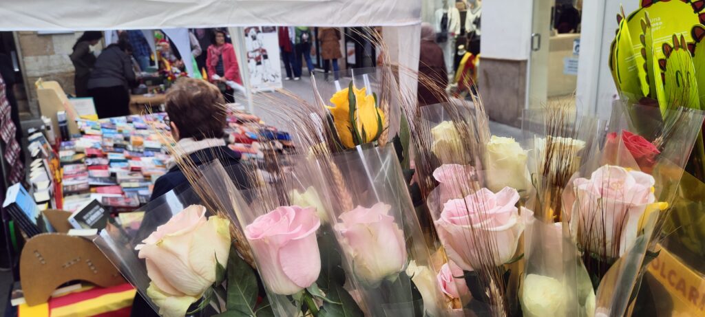 Parada de roses roses i grogues en primer pla amb gent passejant entre llibres al carrer de Sant Blai de Tortosa.