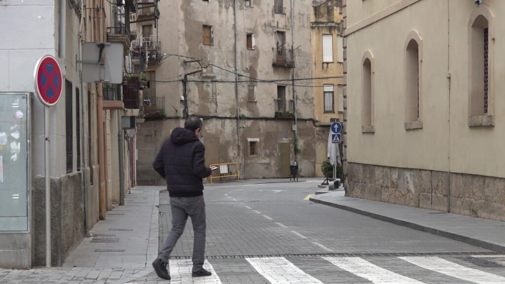 Home caminant per un carrer del nucli antic de Tortosa en direcció a un pas de vianants.