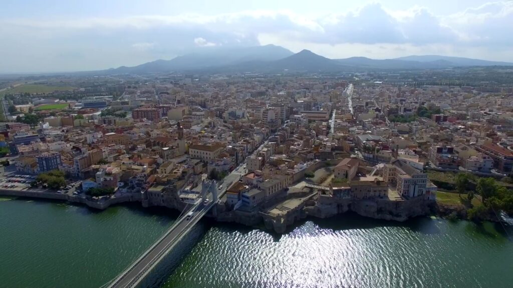 Vista aèria del nucli urbà d'Amposta amb el riu Ebre i el pont penjant en primer pla, Montsià.