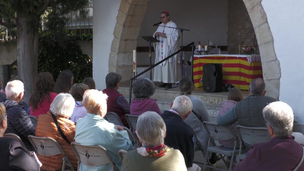 Missa a l'aire lliure oficiada pel bisbe de Tortosa a l'Ermita de la Petja amb assistents asseguts.