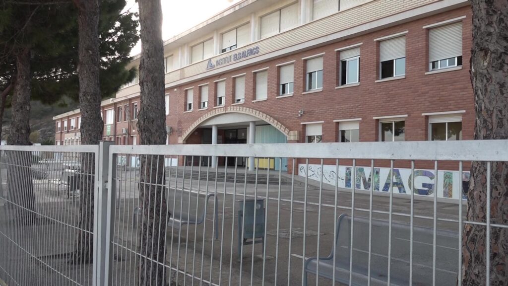 Façana exterior de l'Institut Els Alfacs de la Ràpita, al Montsià, darrere d'un tancat metàl·lic.