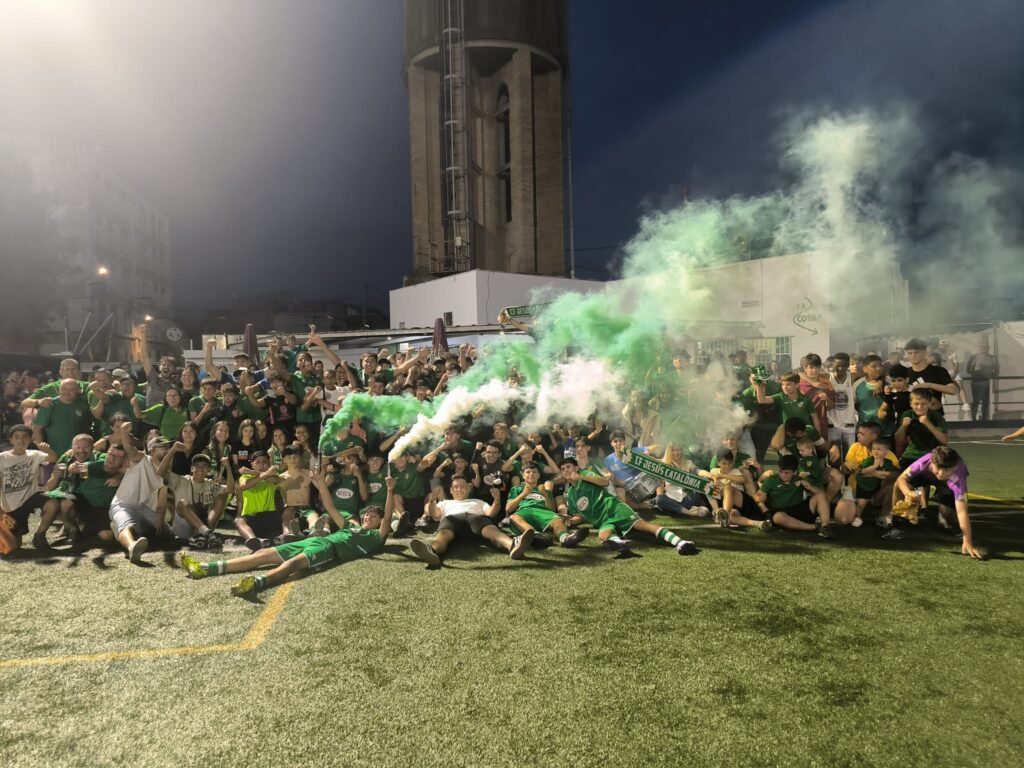 Jugadors i aficionats del CF Jesús Catalònia celebrant l'ascens a Preferent amb fum verd al camp de futbol de la Santa Creu de Jesús, Baix Ebre.