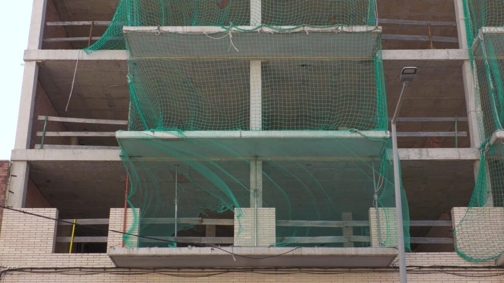 Estructura d'un edificio inacabat de formigó amb xarxes verdes de seguretat a la Ràpita, Montsià