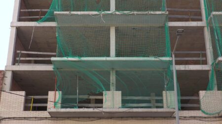 Estructura d'un edificio inacabat de formigó amb xarxes verdes de seguretat a la Ràpita, Montsià