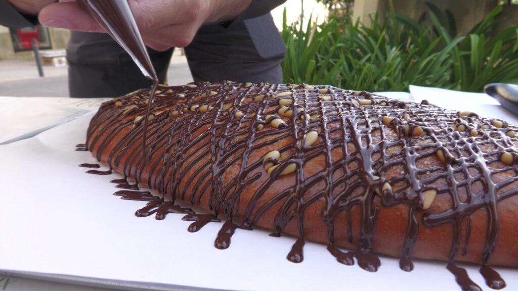 Pastisser aplicant tires de ganes de xocolata negra sobre una coca de Sant Joan artesanal a Flix, Ribera d'Ebre.