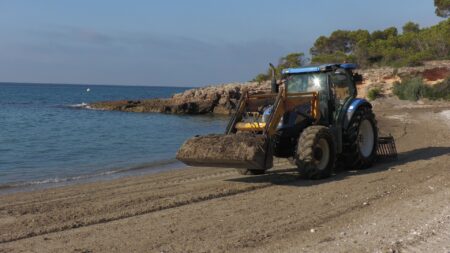 Un tractor realitza tasques de neteja mecànica a la sorra d'una platja de l'Ametlla de Mar.