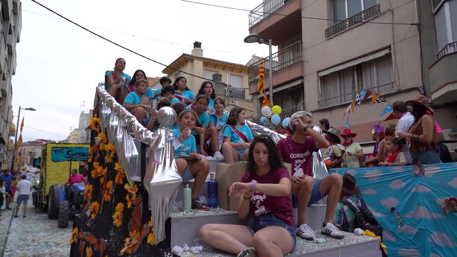 Carrossa engalanada plena de jóvens llançant confeti durant el Gran Cosso Iris de les festes majors de Jesús, Terres de l'Ebre.